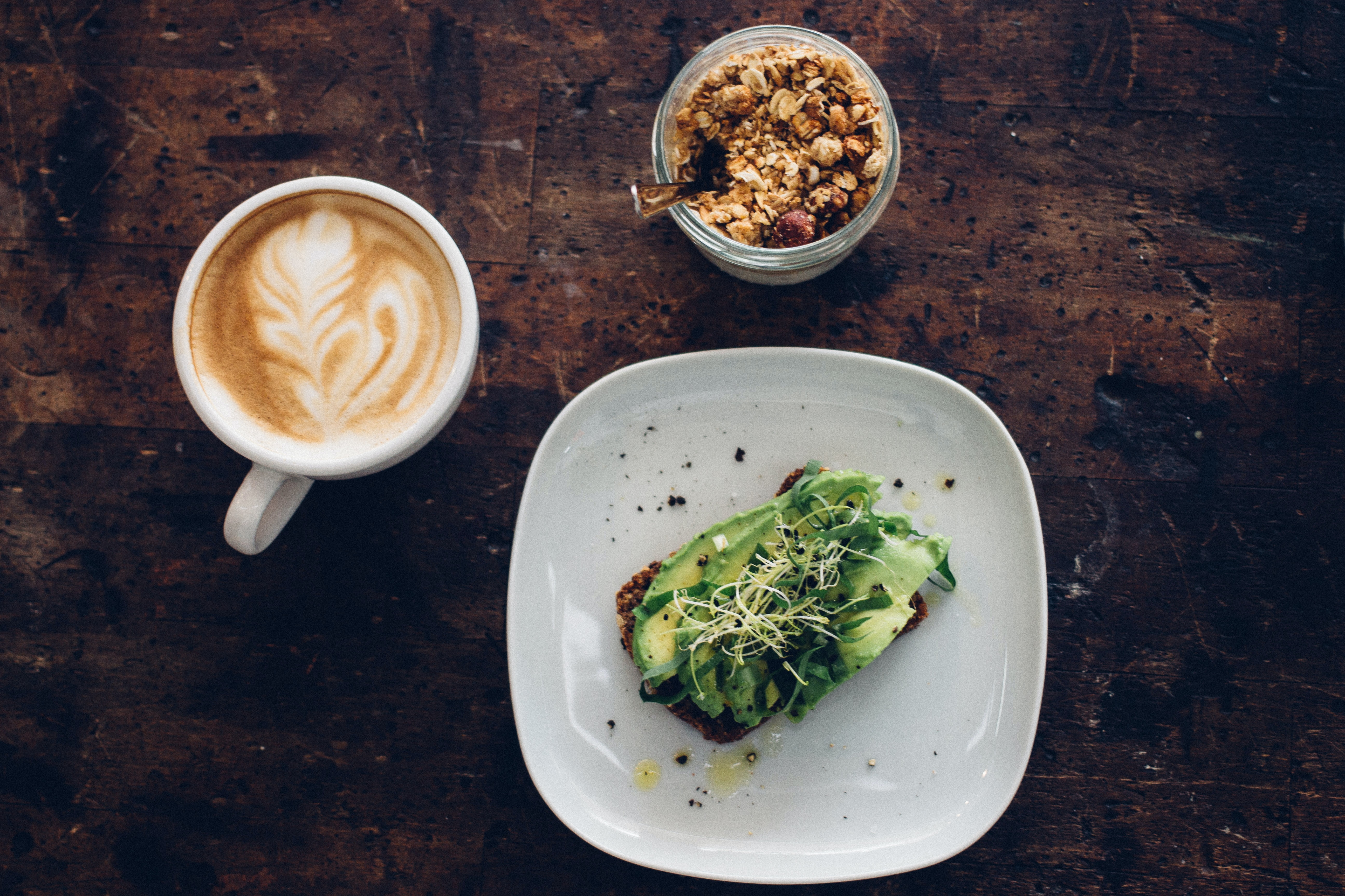 Bird-eye view of avocado toast, hot latte, and yogurt topped with granola.