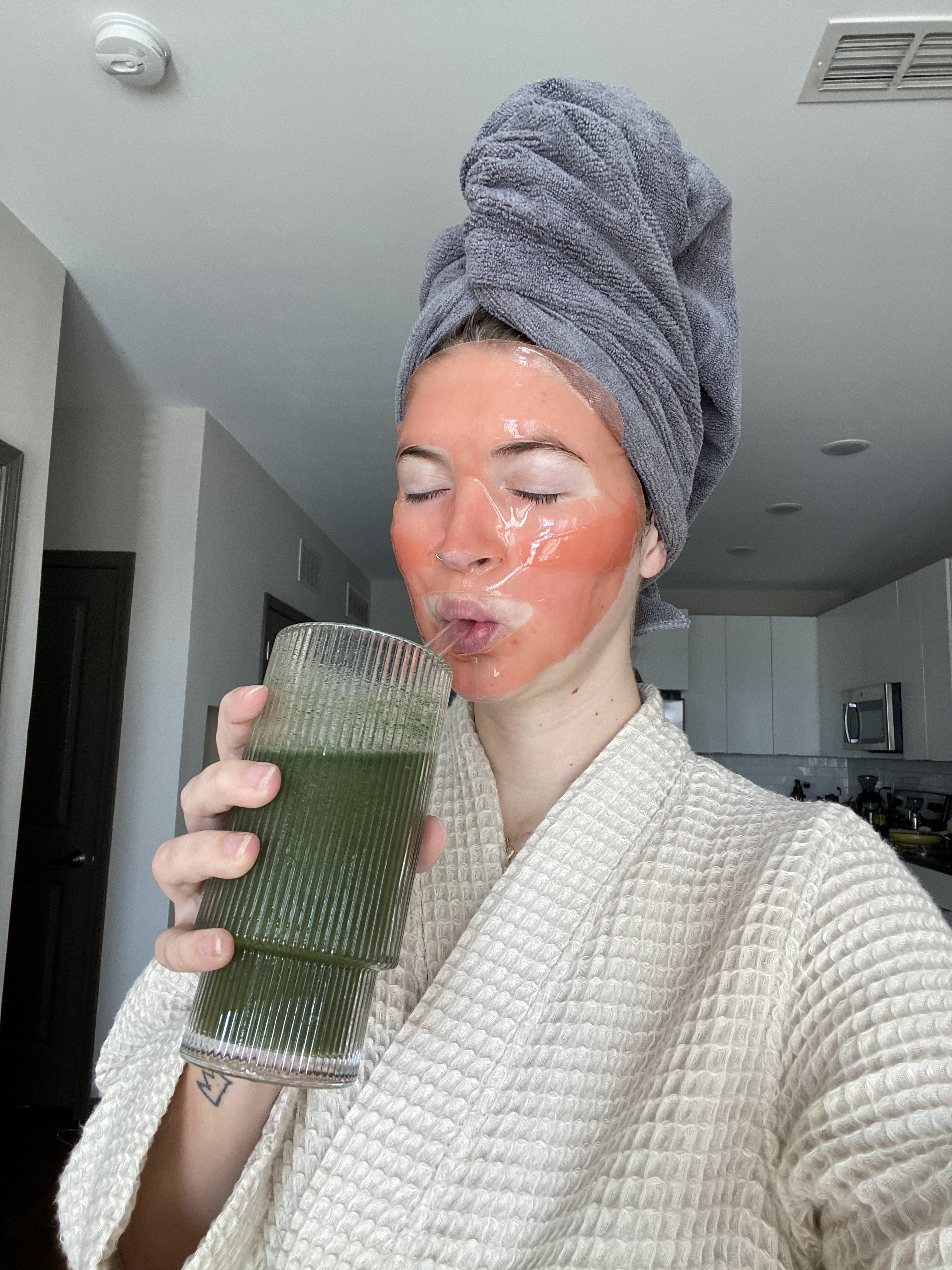 woman with face mask drinking green juice